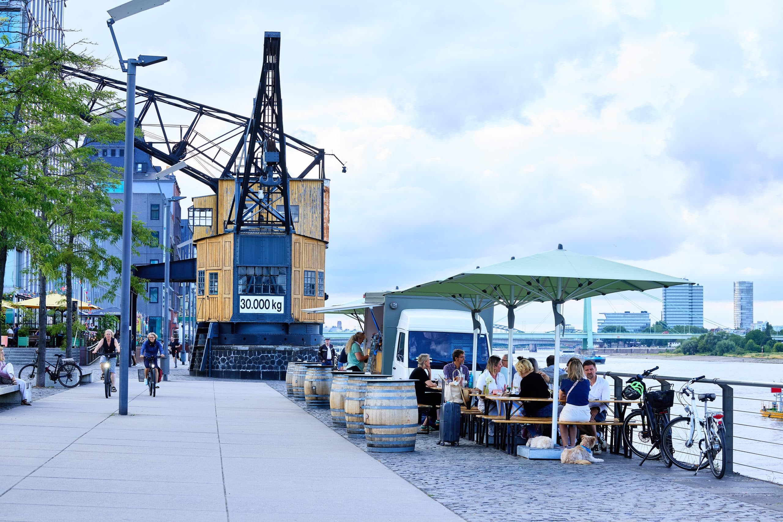 Belebte Hafenpromenade am Deutzer Hafen mit Gastronomie und historischem Kran